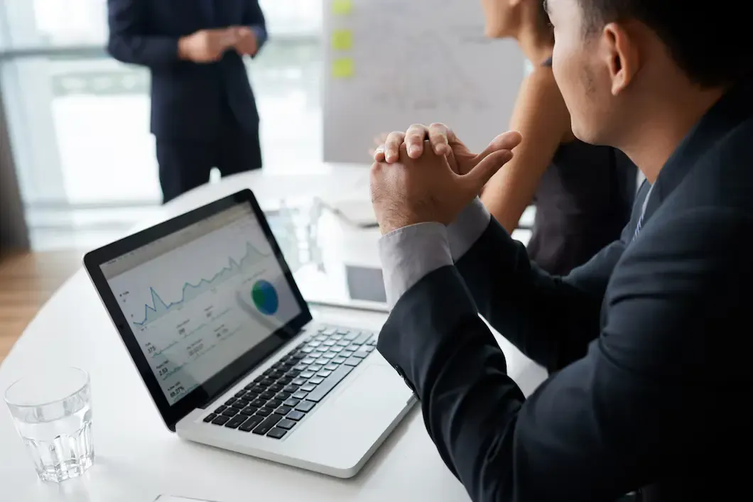 Three professionals in a business meeting, analyzing data on a laptop with graphs and discussing insights